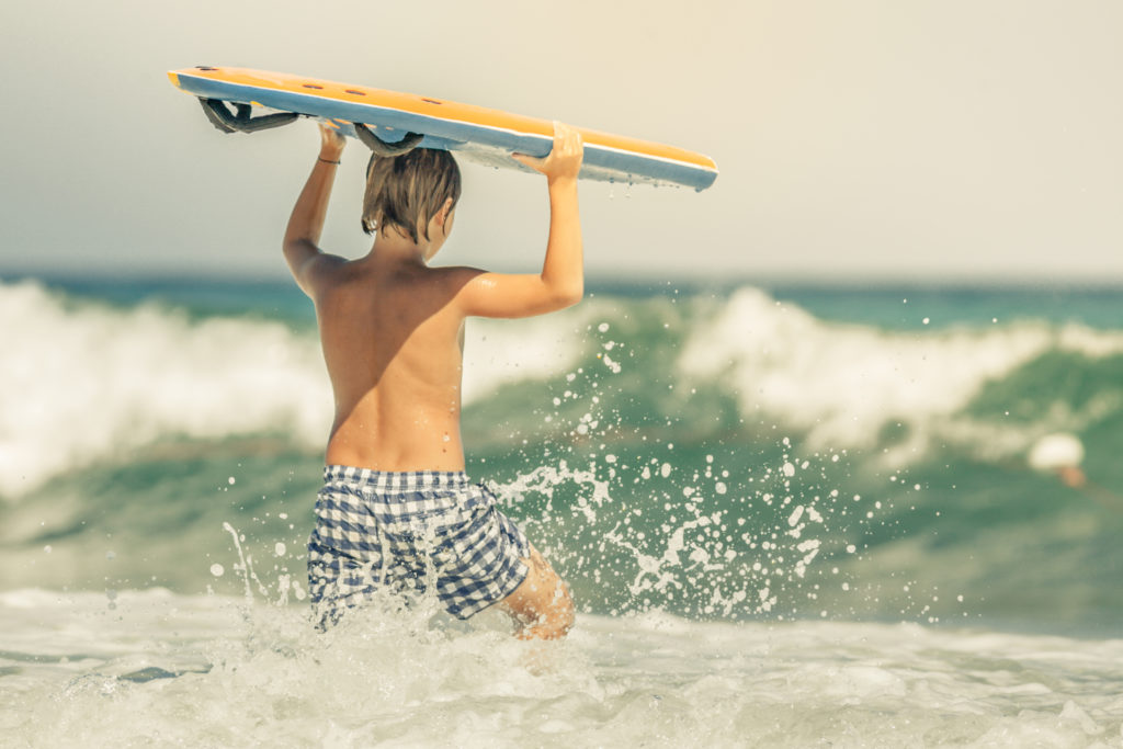 Young boy enjoying the ocean with a surfboard on Folly Beach SC